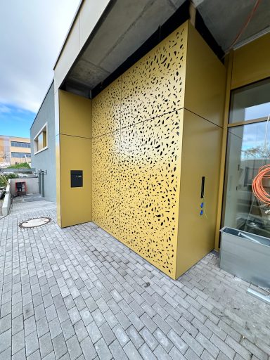 Kita Ingelheim Gelbe Wand mit dekorativem Muster, angrenzend an einen modernen Gebäudeeingang.