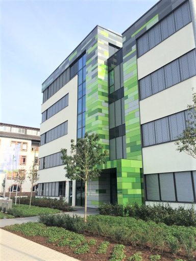 Biontech Mainz Modern Bürogebäude mit grüner und transparenter Fassade, umgeben von Pflanzen.