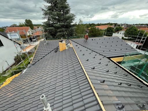 Wohnhaus Lörzweiler Dacharbeiten mit schwarzen Schindeln und Gebäuden im Hintergrund, bewölkter Himmel.